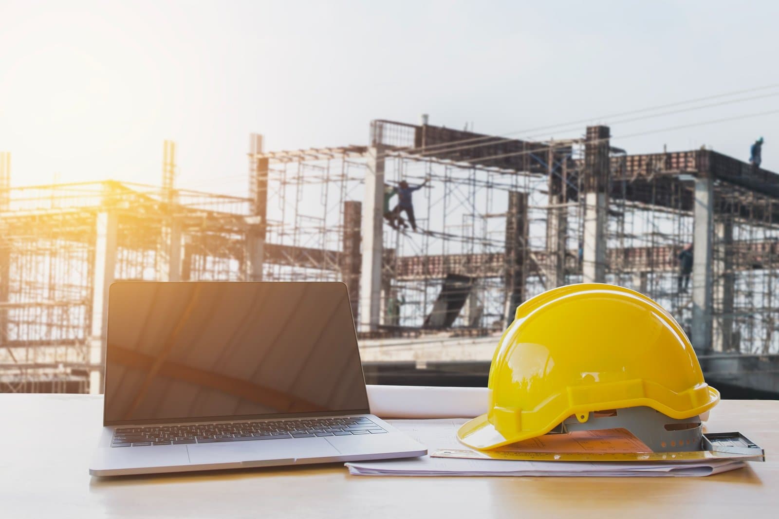 Laptop and hard hat in front of a building under construction